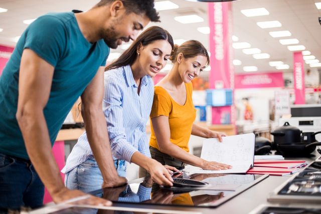 View of a couple and a saleswoman examining a cooktop in an appliance store.