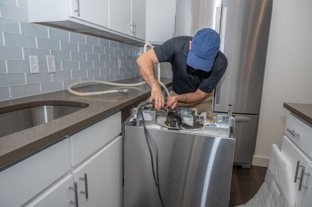 View of a handyman hooking up and installing a dishwasher in a modern kitchen