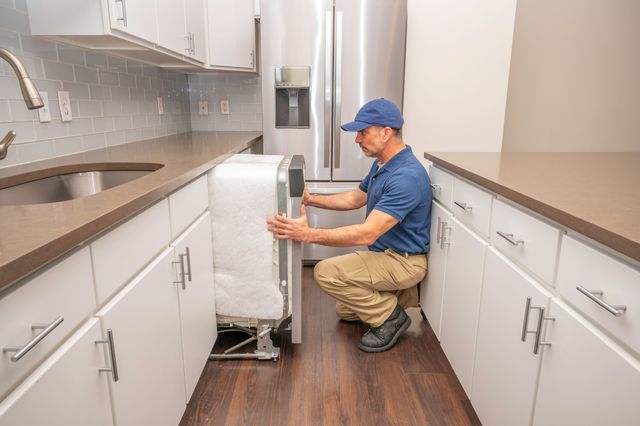 Side view of a man installing a dishwasher in a galley kitchen