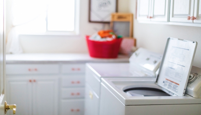 A washing machine sits open in an empty laundry room.