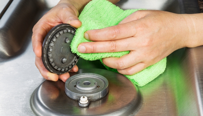 Close-up of someone removing a gas burner cap and wiping things off near the electrodes