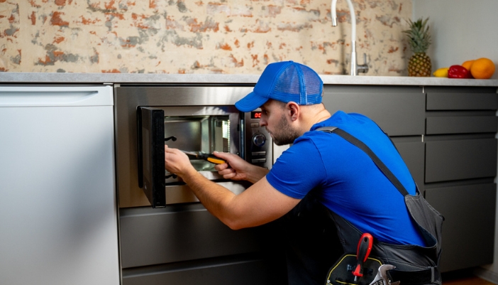 Serv_Repair-vs-Replace-Microwave_3.jpg A service repairman working on a built-in microwave