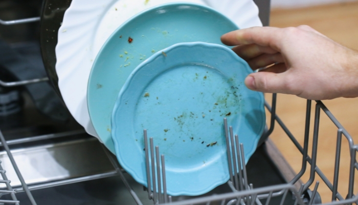 Closeup of someone placing un-rinsed dishes in the dishwasher