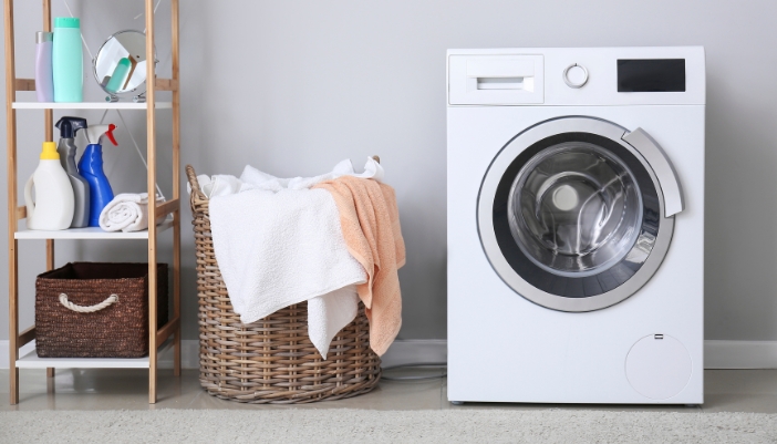 A perfectly level washing machine is next to laundry basket and a shelf full of laundry things