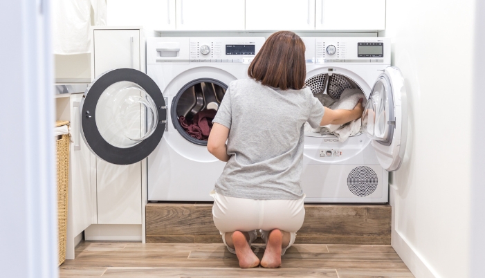 Woman doing the laundry, transferring loads from one machine 