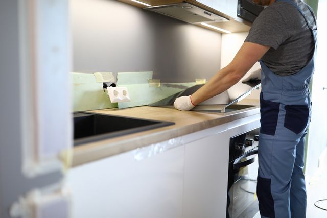 View of a handyman taking a cooktop out of a kitchen countertop as the kitchen gets redone.