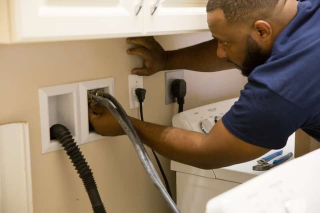 View of a man checking the electrical connections on his washing machine View of a man checking the electrical connections on his washing machine