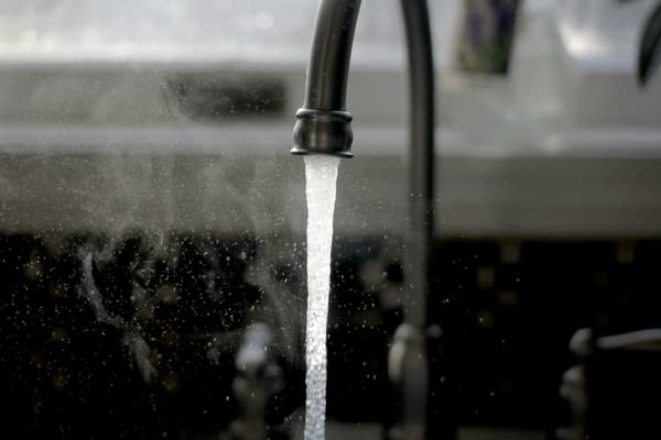 chrome water faucet with a steady stream of water flowing into a sink.