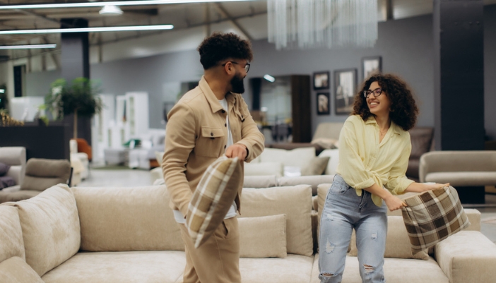 A man and woman pillow fight in a furniture showroom.