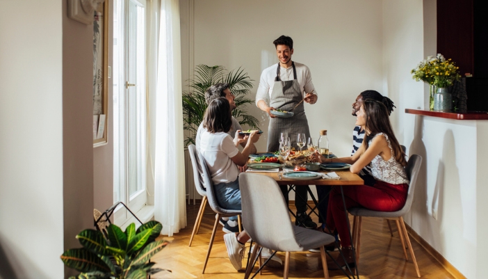 A man hosts his friends at his dining table and serves dinner.