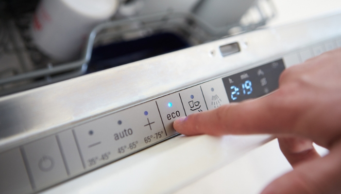 A hand selects eco mode on a dishwasher in their home.