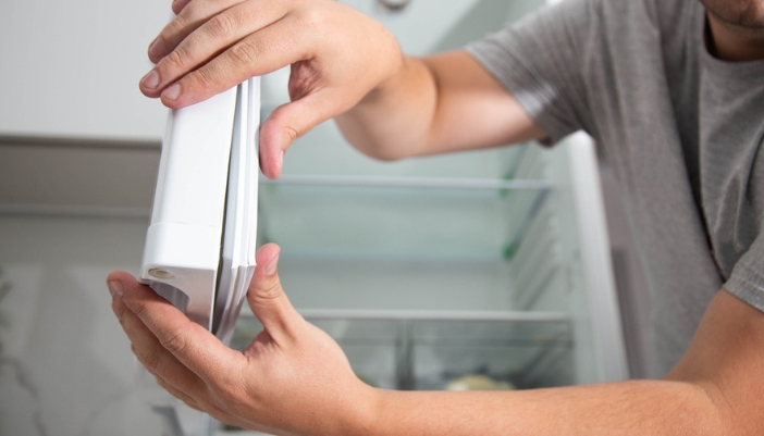 A pair of hands pull at the door seal of a fridge.