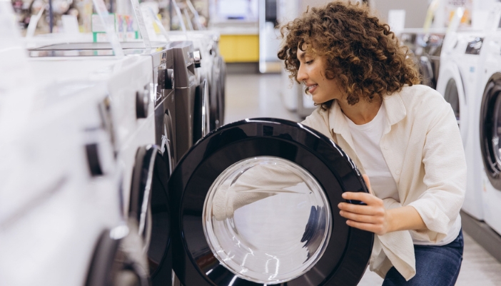 A woman opens a washing machine on an appliance showroom.