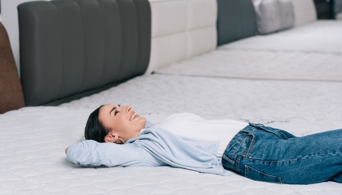 A happy woman lays back on mattresses in a showroom.