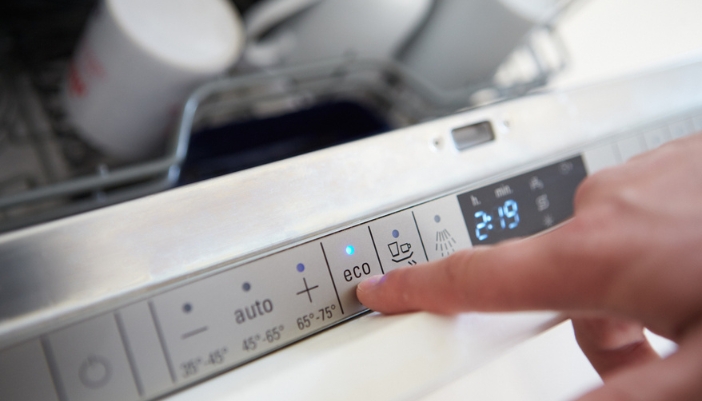A hand selects eco mode on a dishwasher in their home.