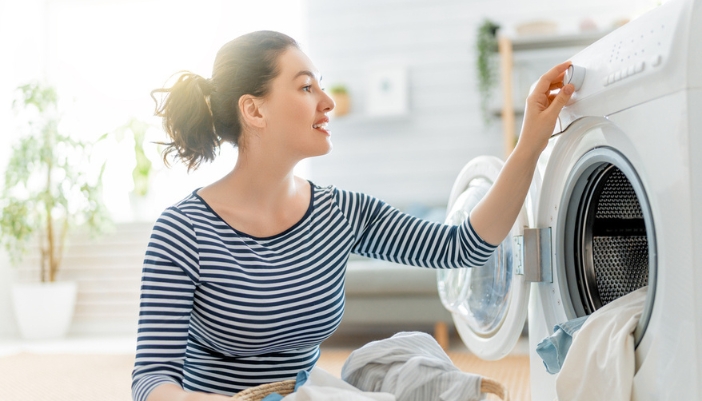 A young woman reaches out to choose a cycle on her washing machine.