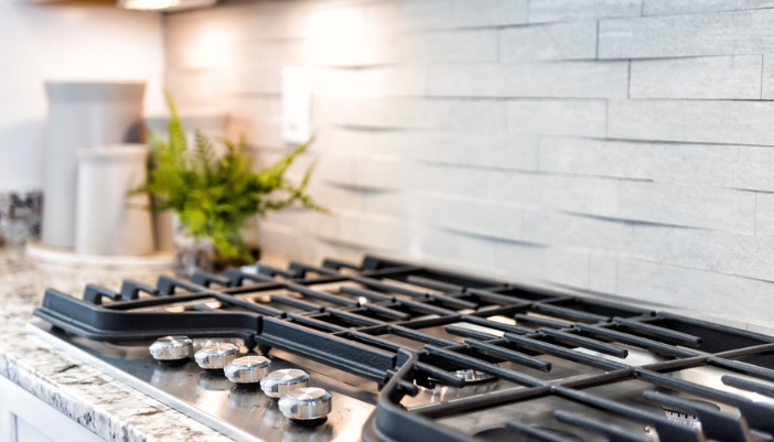 Gas range burner with a blue open flame beneath a stainless steel pan