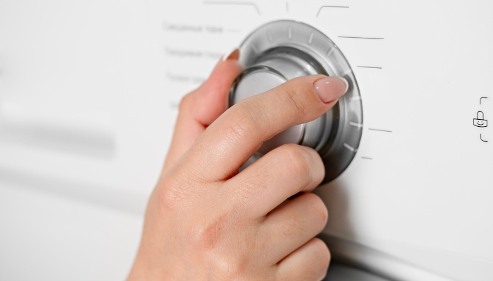A hand turns a knob on a washer to select a cycle.