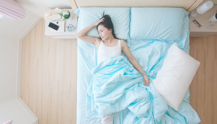 A woman sleeps uncomfortably on her bed at home in a bright room.