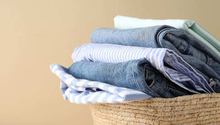 A wicker laundry basket with folded light summer clothing.