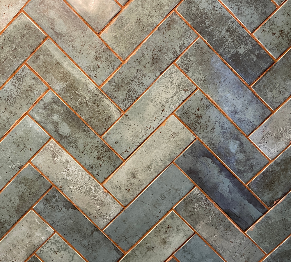 green wall tile installed in herringbone pattern with medium brown grout