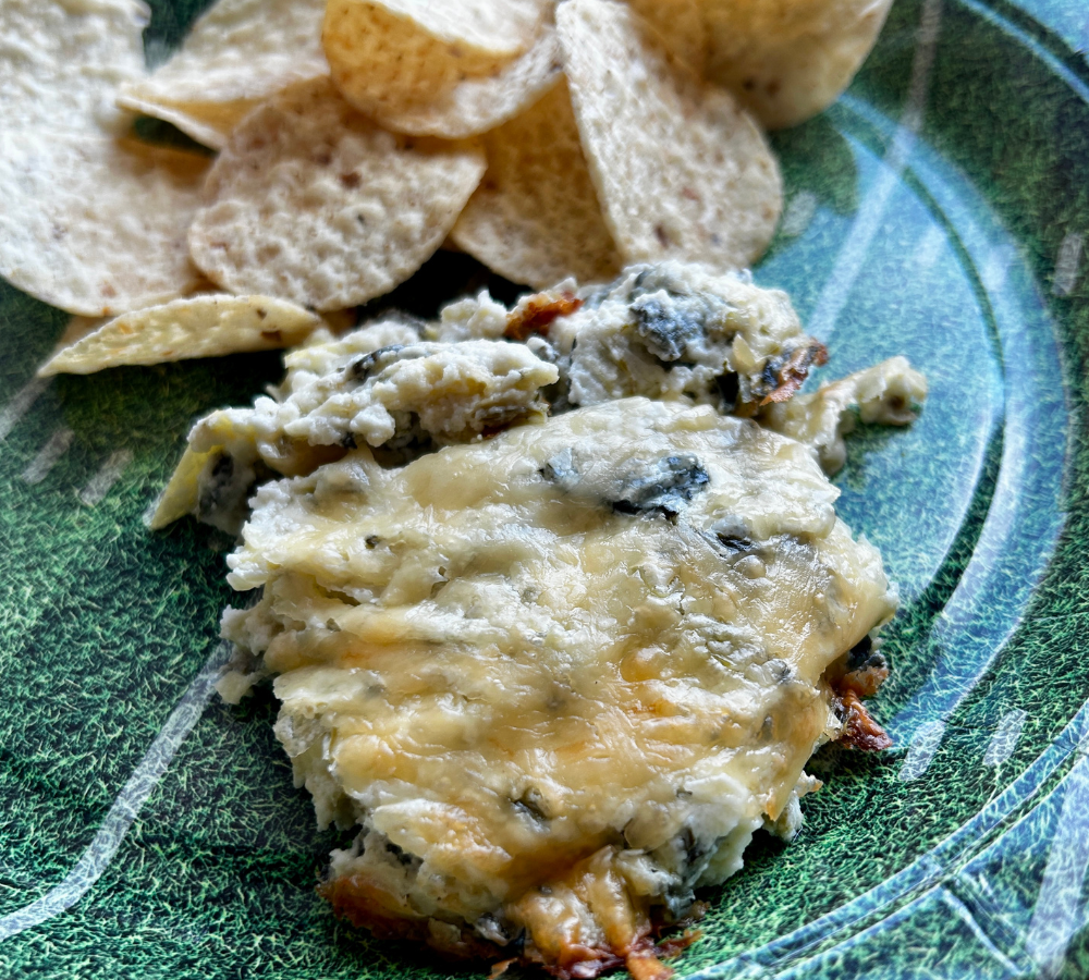 A green plate with baked dip and tortilla chips.