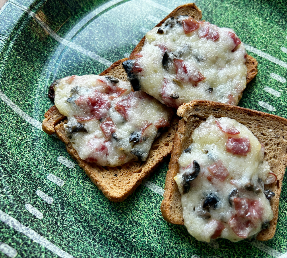 A green plate with mini rye bread and topping.