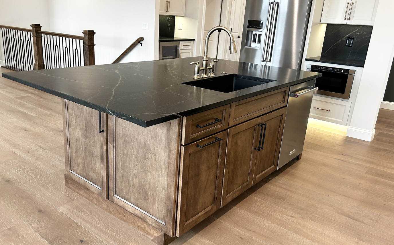 kitchen island cabinetry with maple wood with medium frontier stain applied shown with black counters and undermount sink