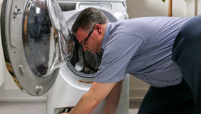 A repairman reaches into a dryer to fix it.