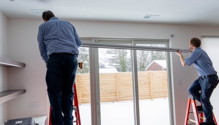 A pair of technicians install smart shades in a modern home.