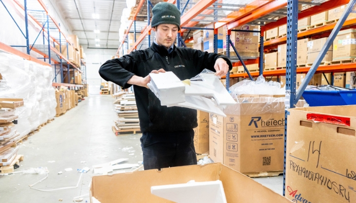 A man rips up styrofoam materials in a warehouse.
