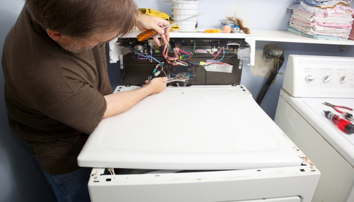 A man looks at wires and troubleshoots his broken dryer.