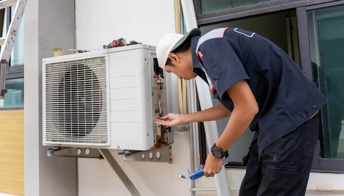 Technician adjusting the wiring on an outdoor through-the-wall air conditioner condenser unit