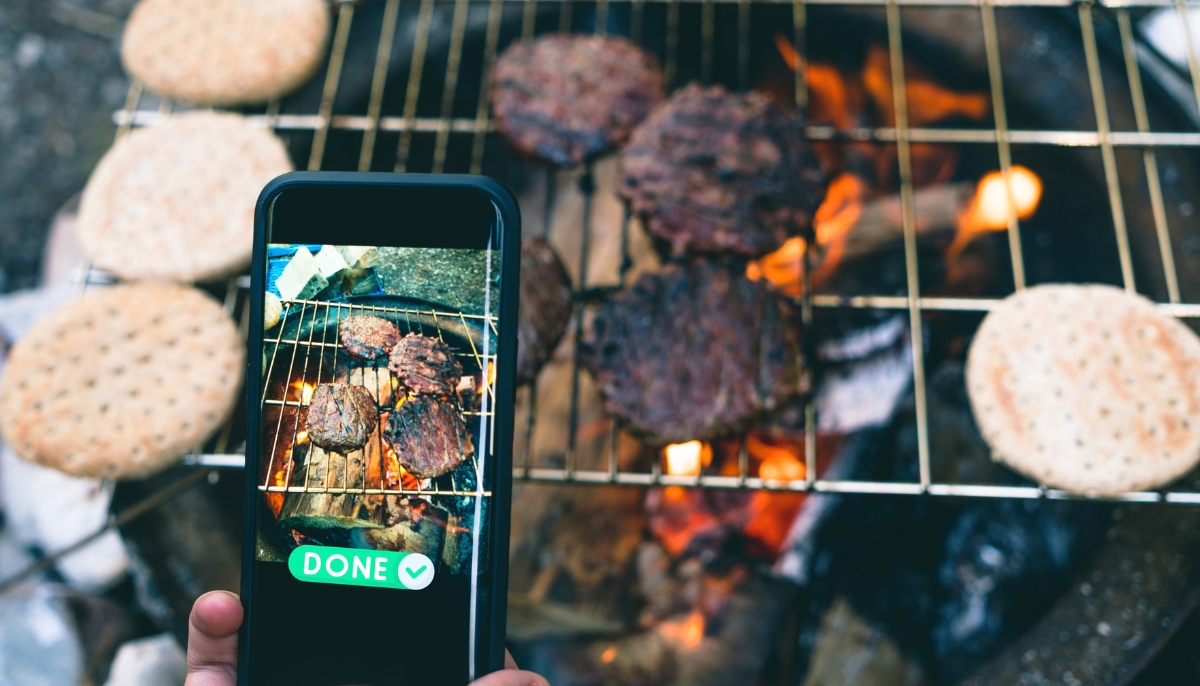 A backyard griller checking a smart grill's temperature readings on a smartphone app