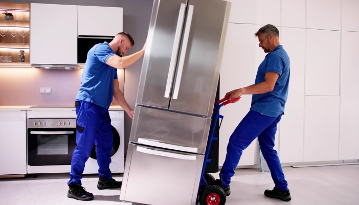 Two delivery men bring a new fridge into a home's kitchen.