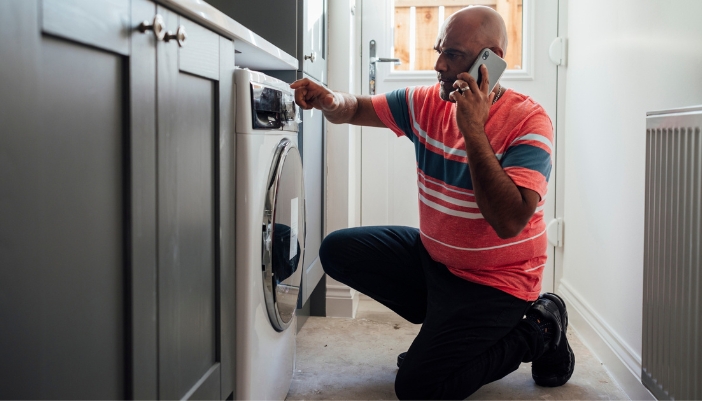 A man on the phoen looks at the functions on his washer.
