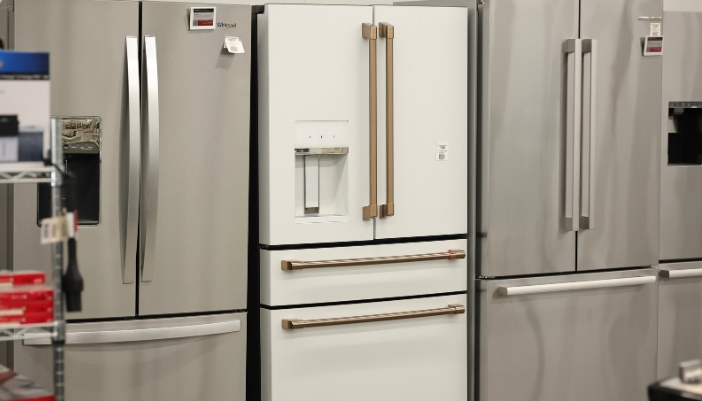 White French door refrigerator with bronze handles and an external water and ice dispenser, displayed between stainless steel models in an appliance showroom