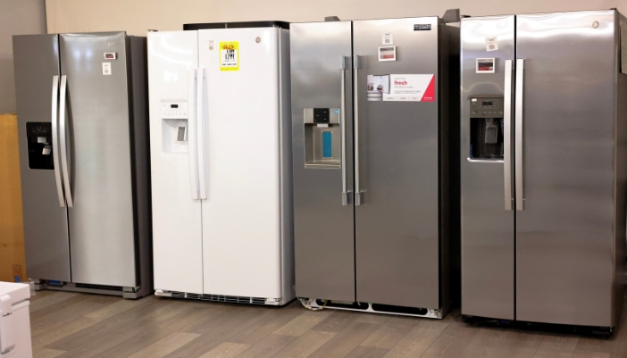 Row of white and stainless steel side-by-side refrigerators with external water and ice dispensers in an appliance showroom