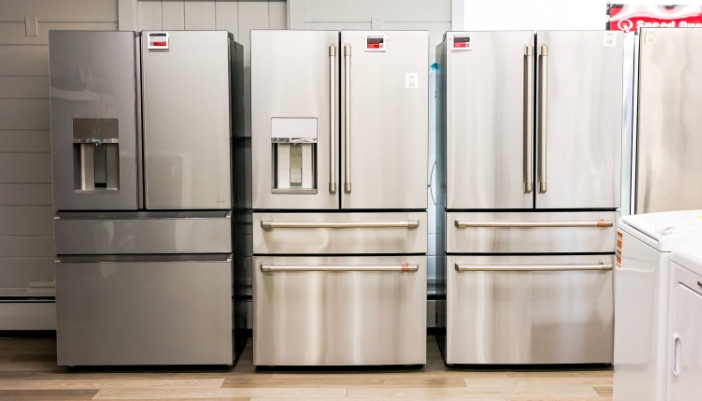 Stainless steel French door refrigerators in a showroom, two with external water and ice dispensers and one with a seamless, dispenser-free door