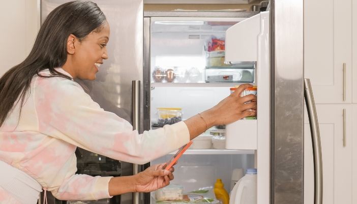 A young woman reaches into her fridge at home.