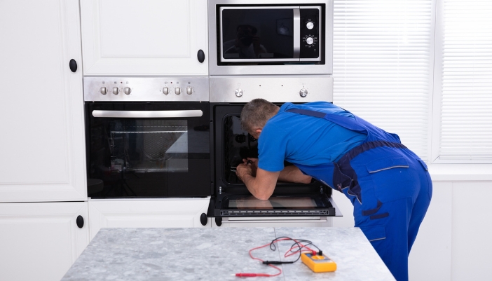 An appliance repair man reaches into a set of wall ovens.