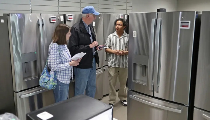 An appliance salesman walks a couple through fridge options.