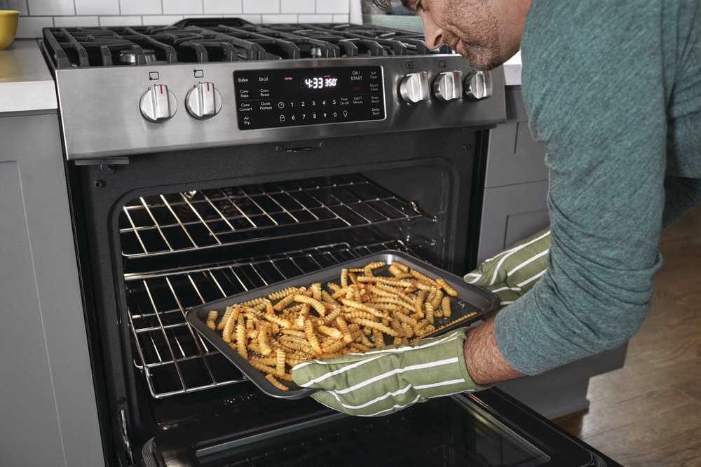 Man takes a tray of crinkle fries out of Frigidaire Gallery FGGH3047VF range oven
