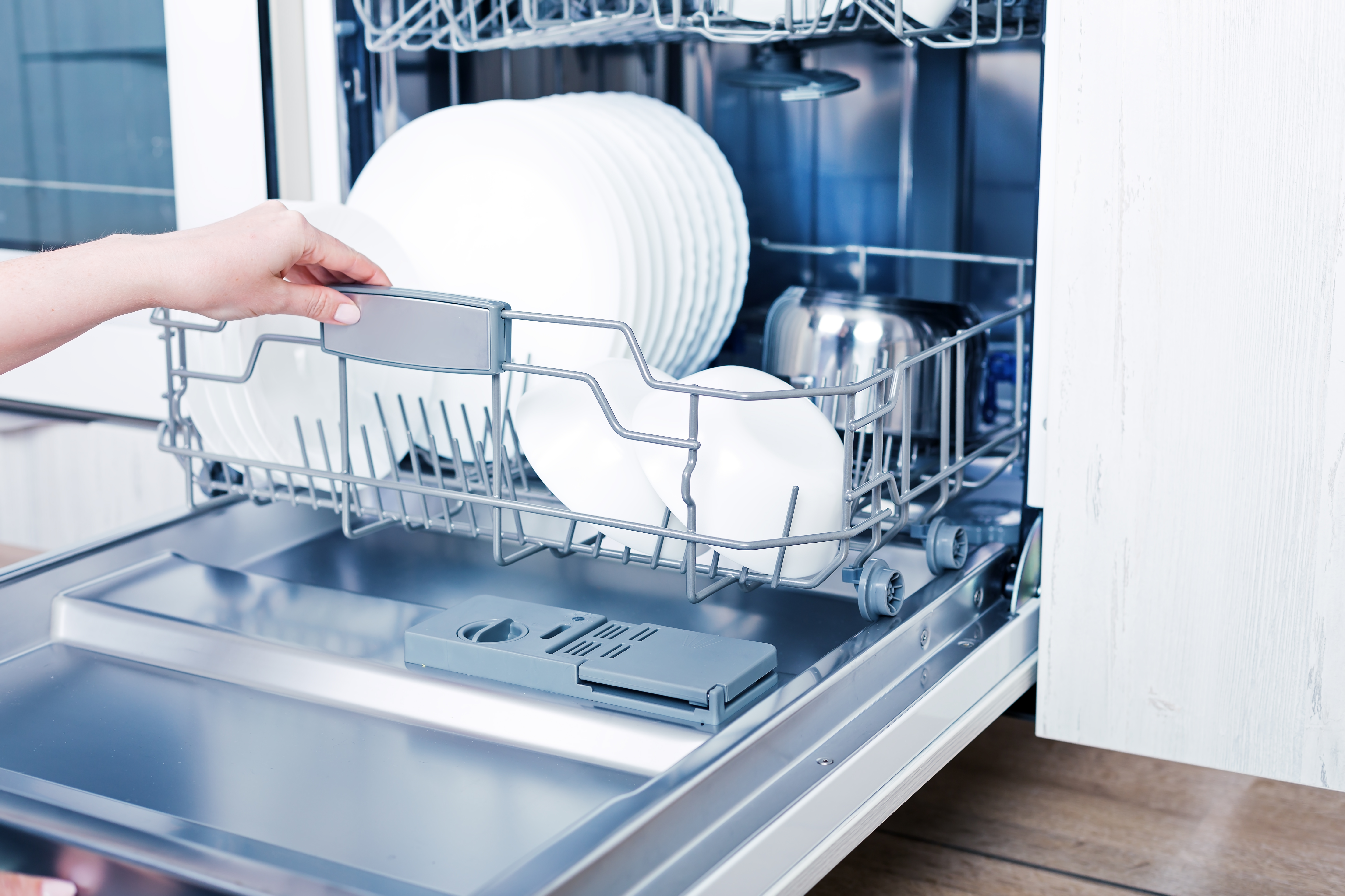 Woman grabs fully loaded bottom rack of dishwasher with stainless steel tub 