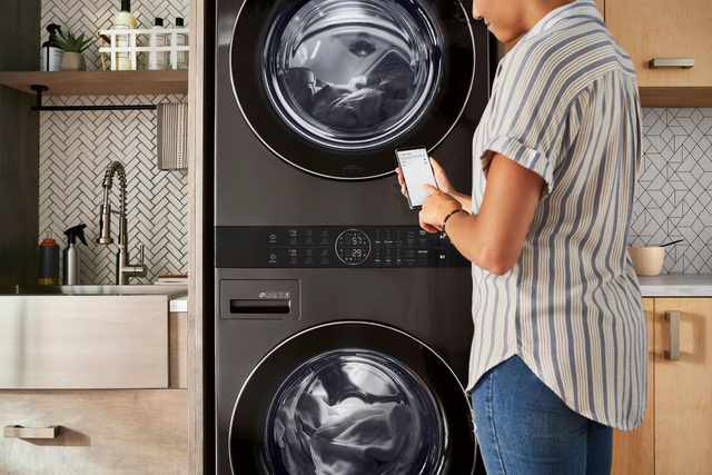 View of a woman reading a notification from her LG ThinQ app in front of her LG washer and dryer