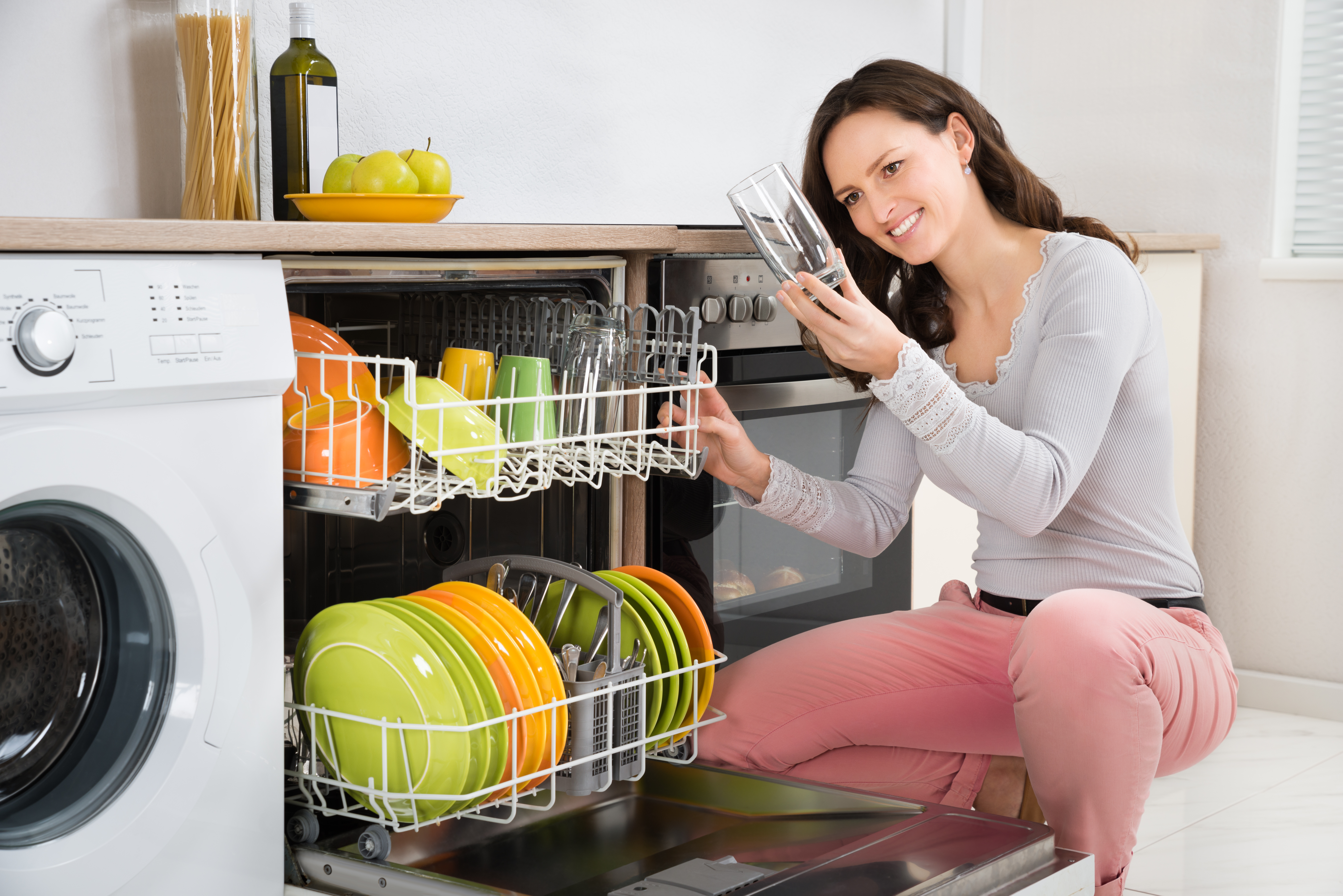 Casually dressed smiling woman checks a glass from a dishwasher