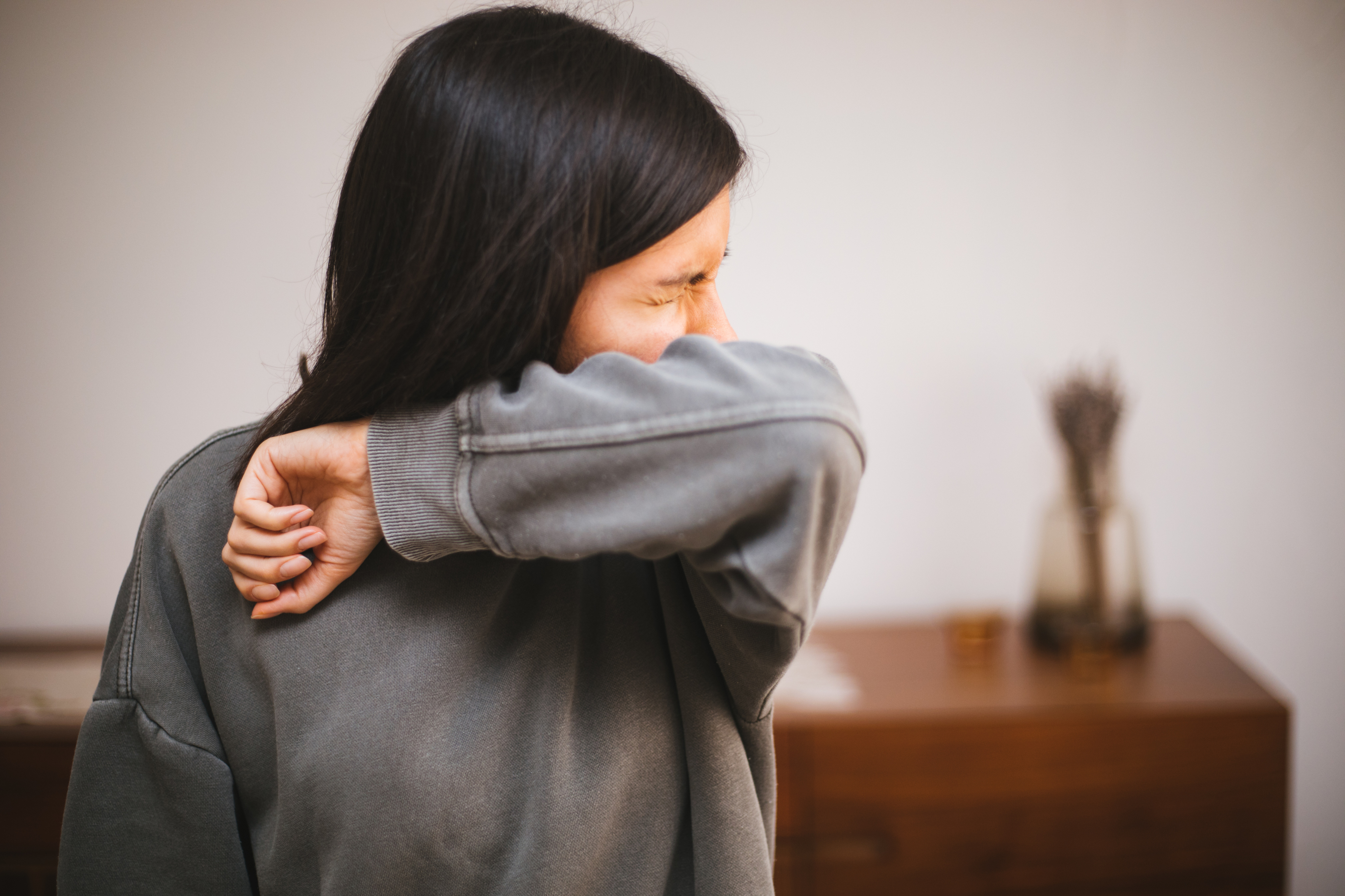 Woman in gray sweatshirt sneezes into elbow