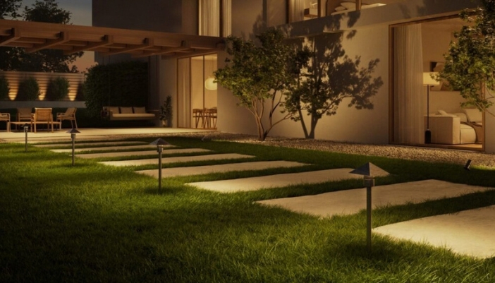 Path lights lining stone stepping pavers across a lawn toward a softly lit modern home and patio at dusk