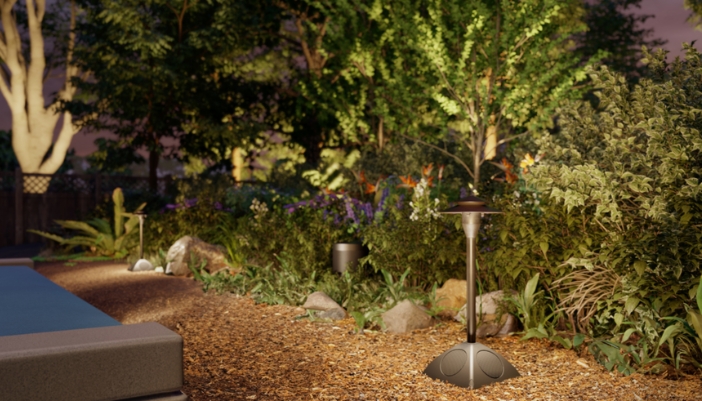 Outdoor landscape speaker and path light set among illuminated garden plantings beside a pool at dusk