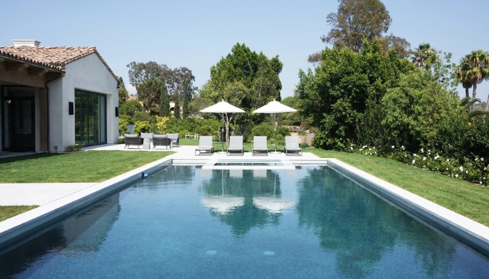 An outdoor residential pool with white poolside furniture.